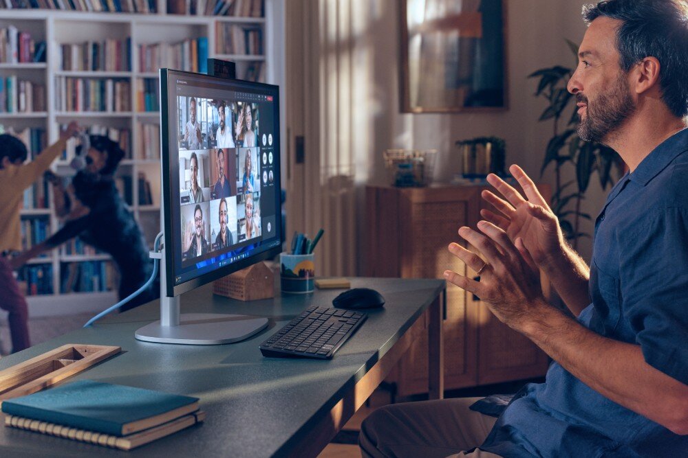 Komputer All in One HP EliteStudio 8 G1I SL Mężczyzna siedzący przy biurku w domu, gestykulujący podczas rozmowy wideo widocznej na dużym monitorze, w tle regał z książkami, kamera, rozdzielczość, funkcja IR