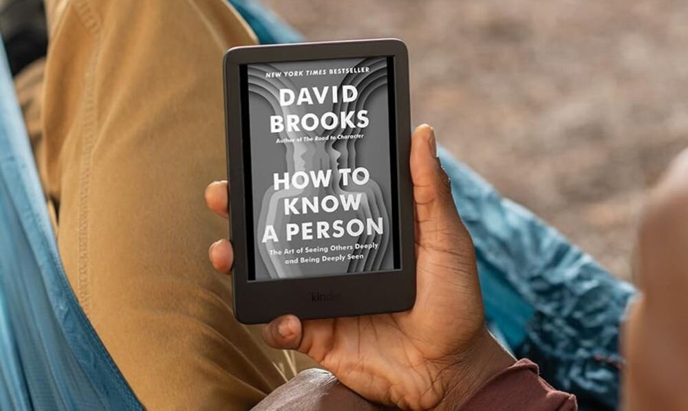 Osoba trzyma czytnik e-booków z wyświetloną okładką książki \'HOW TO KNOW A PERSON\' autorstwa Davida Brooksa. Czytnik ma czarną ramkę i wyraźny ekran.