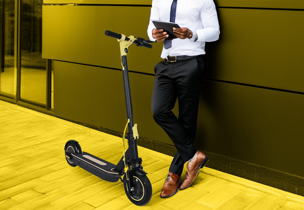 Hulajnoga elektryczna XRIDER M10 ME 65km 500W Amortyzacja 10 cali Czarny mężczyzna sti oparty o ścianę obok hulajnoga wsparta na stopce składana stopka wytrzymała nóżka w centralnym punkcie ciężkości