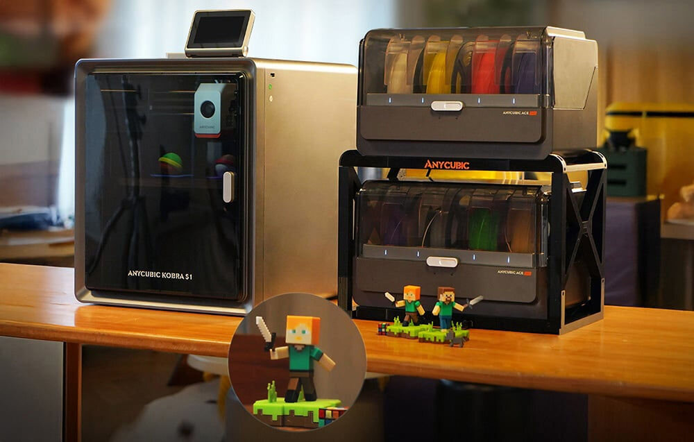 Na drewnianym stole znajduje się drukarka 3D ANYCUBIC Kobra S1 oraz dwa pojemniki z filamentami w różnych kolorach. Obok widoczna jest figurka postaci z mieczem świetlnym na zielonej podstawce.