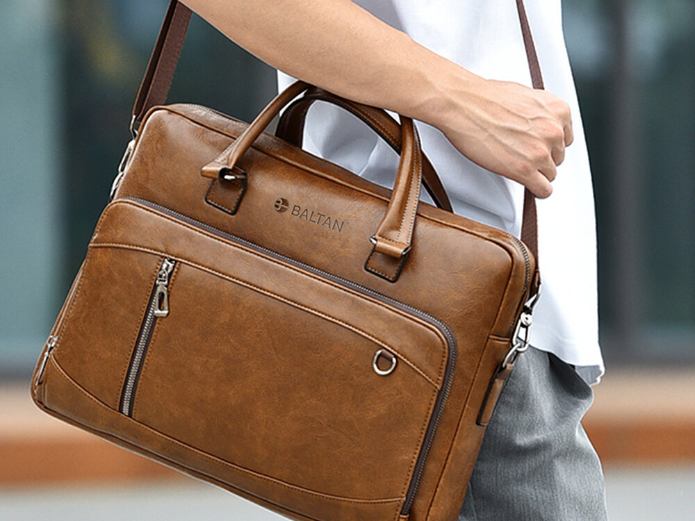 Torba na laptopa BALTAN Office 15.6 cali Mężczyzna w białej koszulce i szarych spodniach niesie na ramieniu brązową torbę na laptopa marki Baltan, z widocznymi uchwytami i przednią kieszenią zamykaną na zamek błyskawiczny.