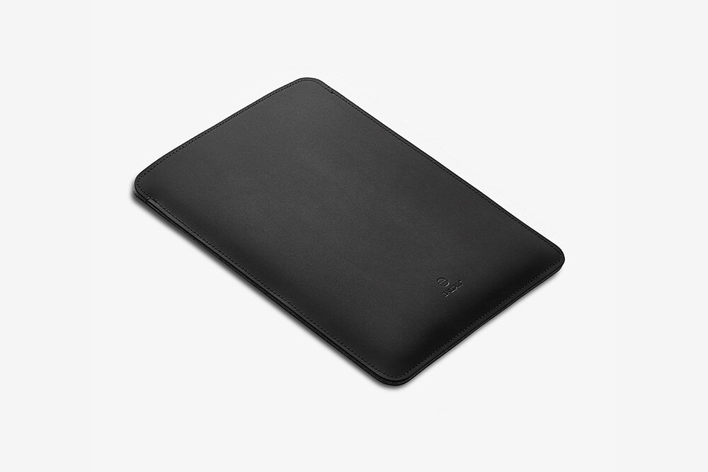 Etui na laptopa BALTAN Sleeve do Apple MacBook Air M4 15.3 cali Czarny łatwość czyszczenia prostota pielęgnacja Kobieta w ceglastoczerwonej sukience siedzi na ławce na zewnątrz, trzymając czarne skórzane etui na laptopa. Widoczny jej tors, ręce i twarz częściowo zwrócona w bok.