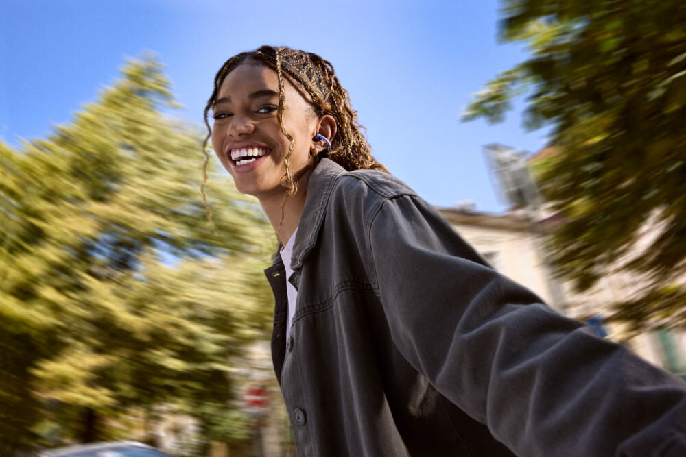 Słuchawki powietrzne JBL Soundgear Clips z etui ładującym i portem USB-C, osoba z założonymi słuchawkami na świeżym powietrzu