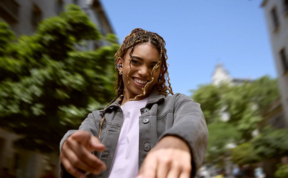 Słuchawki powietrzne JBL Soundgear Clips z przetwornikiem 11 mm i Adaptive Bass Boost, osoba z założonymi słuchawkami na świeżym powietrzu