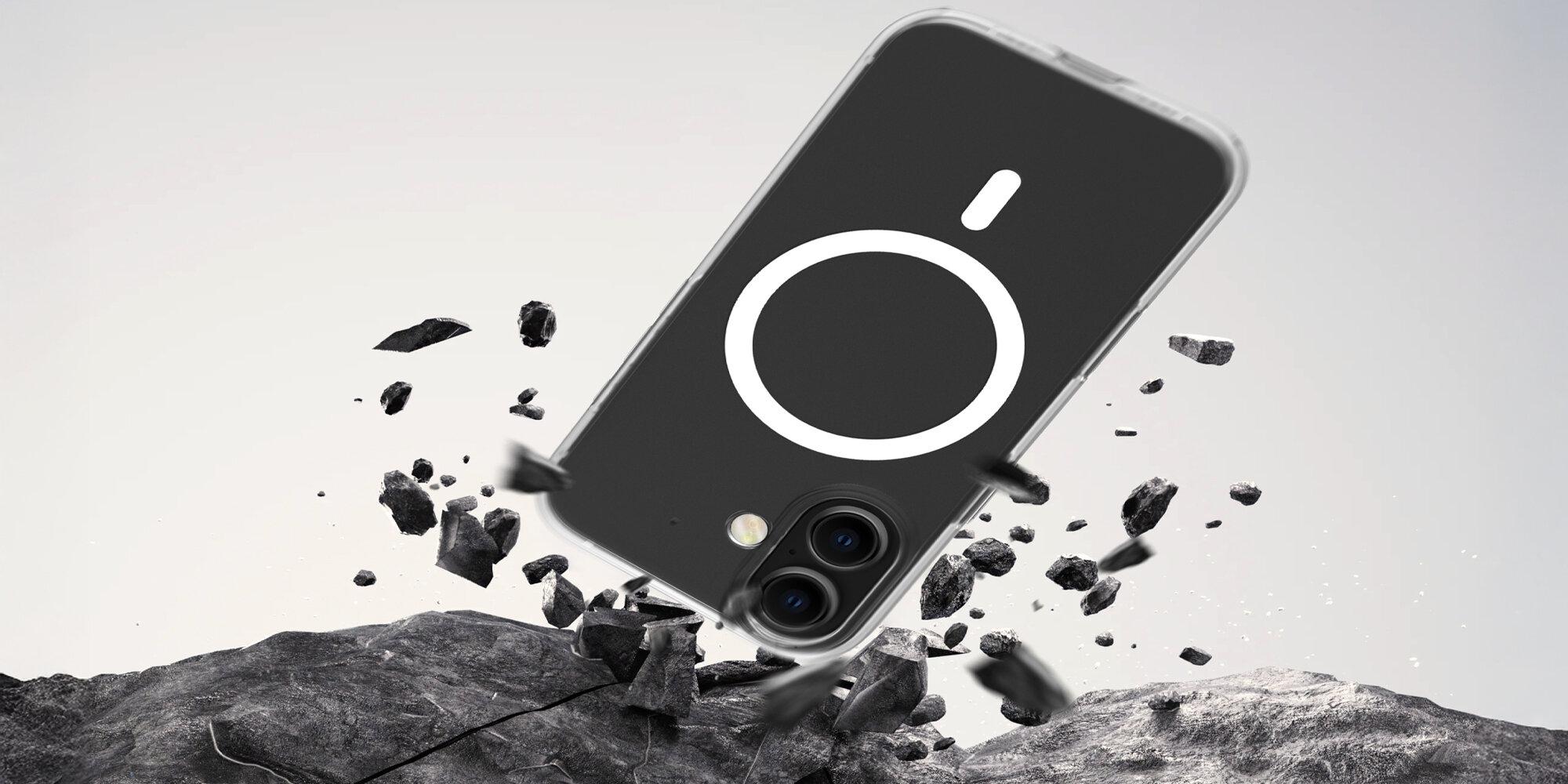 Smartfon w przezroczystym etui uderzający o kamieniste podłoże, widoczne unoszące się odłamki symbolizujące test upadku