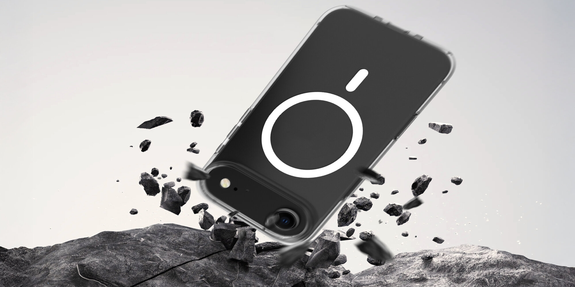 Smartfon w przezroczystym etui uderzający o kamieniste podłoże, widoczne unoszące się odłamki symbolizujące test upadku