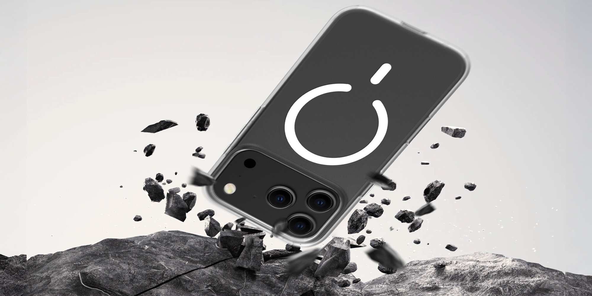 Smartfon w przezroczystym etui uderzający o kamieniste podłoże, widoczne unoszące się odłamki symbolizujące test upadku