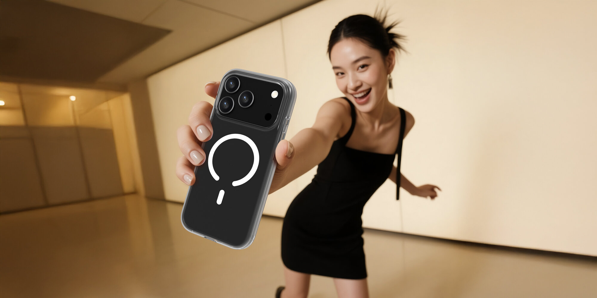 Uśmiechnięta kobieta pokazuje do kamery trzymany w dłoni smartfon w etui. W tle pomieszczenie w ciepłych barwach.