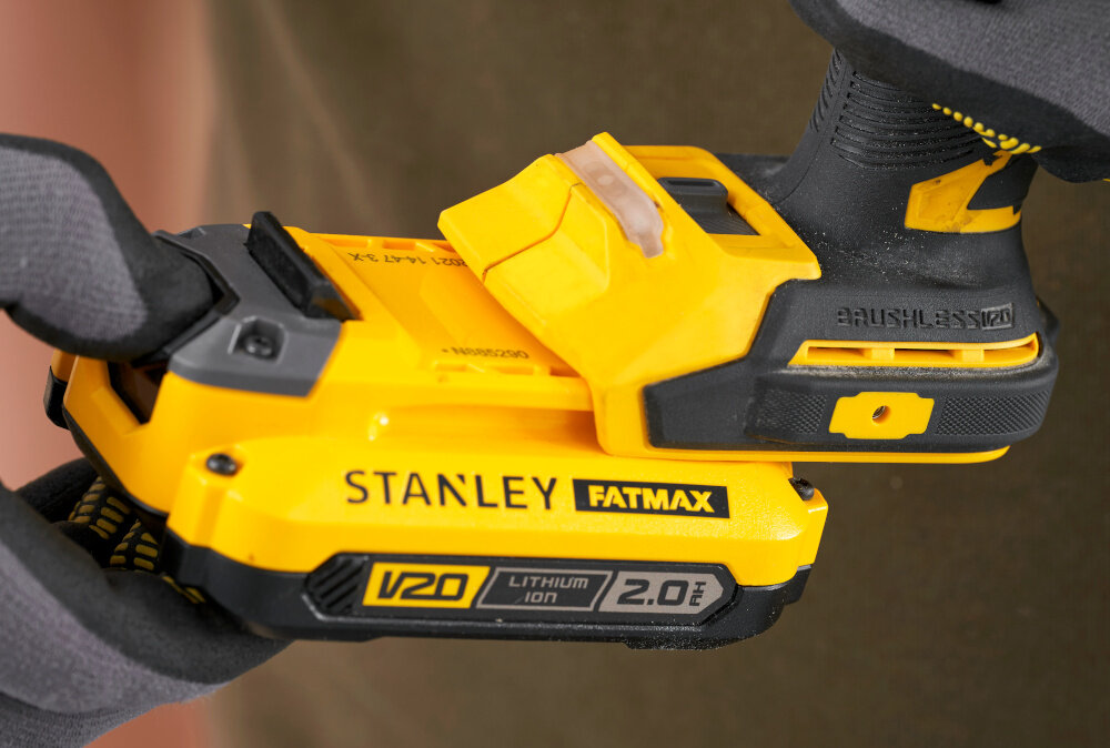 Zestaw elektronarzędzi STANLEY Fatmax SFMCK211D2T-QW zbliżenie na akumulator osoba wkłada akumulator w narzędzie w tle drewniana ściana akumulatory z systemu V20 jedna bateria w wielu narzędziach stabilne zasilanie dwie baterie o pojemności 2,0 Ah każda ładowarka