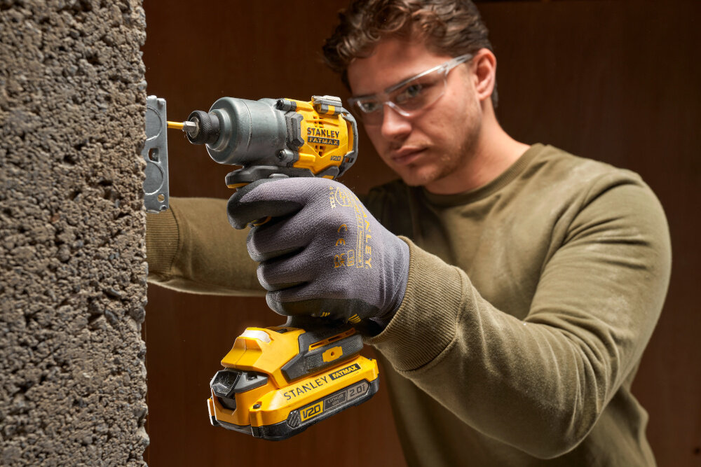 Zestaw elektronarzędzi STANLEY Fatmax SFMCK211D2T-QW pomieszczenie osoba trzyma zakrętarkę w dłoni wierci w betonowej ścianie zakrętarka STANLEY SFMCF830 wydajny silnik mechanizm udarowy do 3200 obr./min, 4200 udarów/min i 200 Nm momentu obrotowego radzi sobie z mocnymi wkrętami i wymagającymi połączeniami