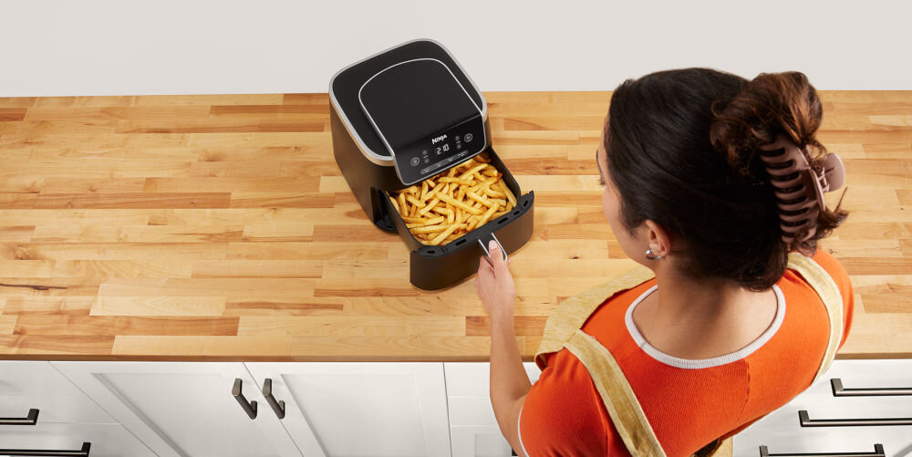 Air Fryer Frytkownica beztłuszczowa NINJA AF140EU frytkownica stoi na blacie czarna obudowa kobieta otwiera szufladę w szufladzie frytki jedno naciśnięcie przycisku ustawienie programu temperatury czasu działania szeroki zakres temperatur od 40 do 210 stopni delikatne podgrzanie resztek obiadu Precyzyjna regulacja temperatury optymalne efekty kulinarne