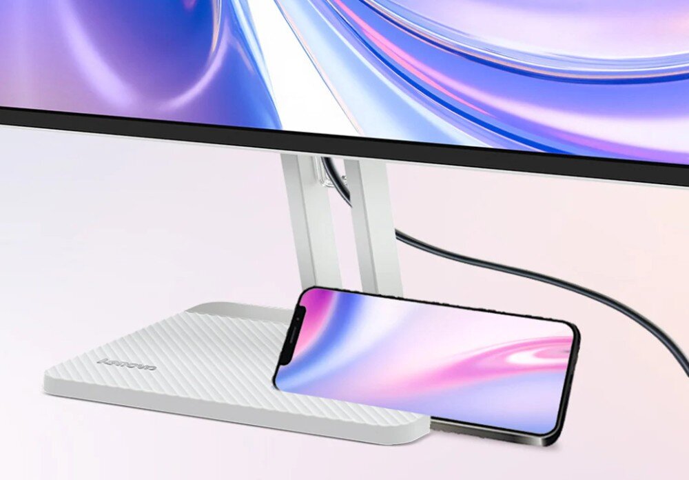 Monitor z cienką ramką, pod którym leży smartfon z kolorowym ekranem. Na podstawie monitora widoczne jest logo \'Lenovo\'.