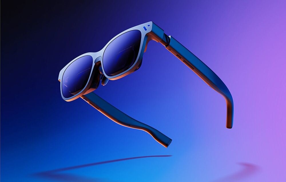 Okulary przeciwsłoneczne z ciemnymi szkłami i białą oprawką, zawieszone na tle w odcieniach niebieskiego i fioletowego. Widoczne są zauszniki o ciemniejszym kolorze.