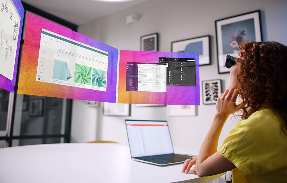 Okulary VITURE XR Luma Czarny Kobieta w żółtej koszuli siedzi z laptopem przy biurku i ma nałożone okulary VR wyświetlające 3 ekrany wirtualny ekran system audio Harman bogate detale dźwiękowe brzmienie współgra z obrazem