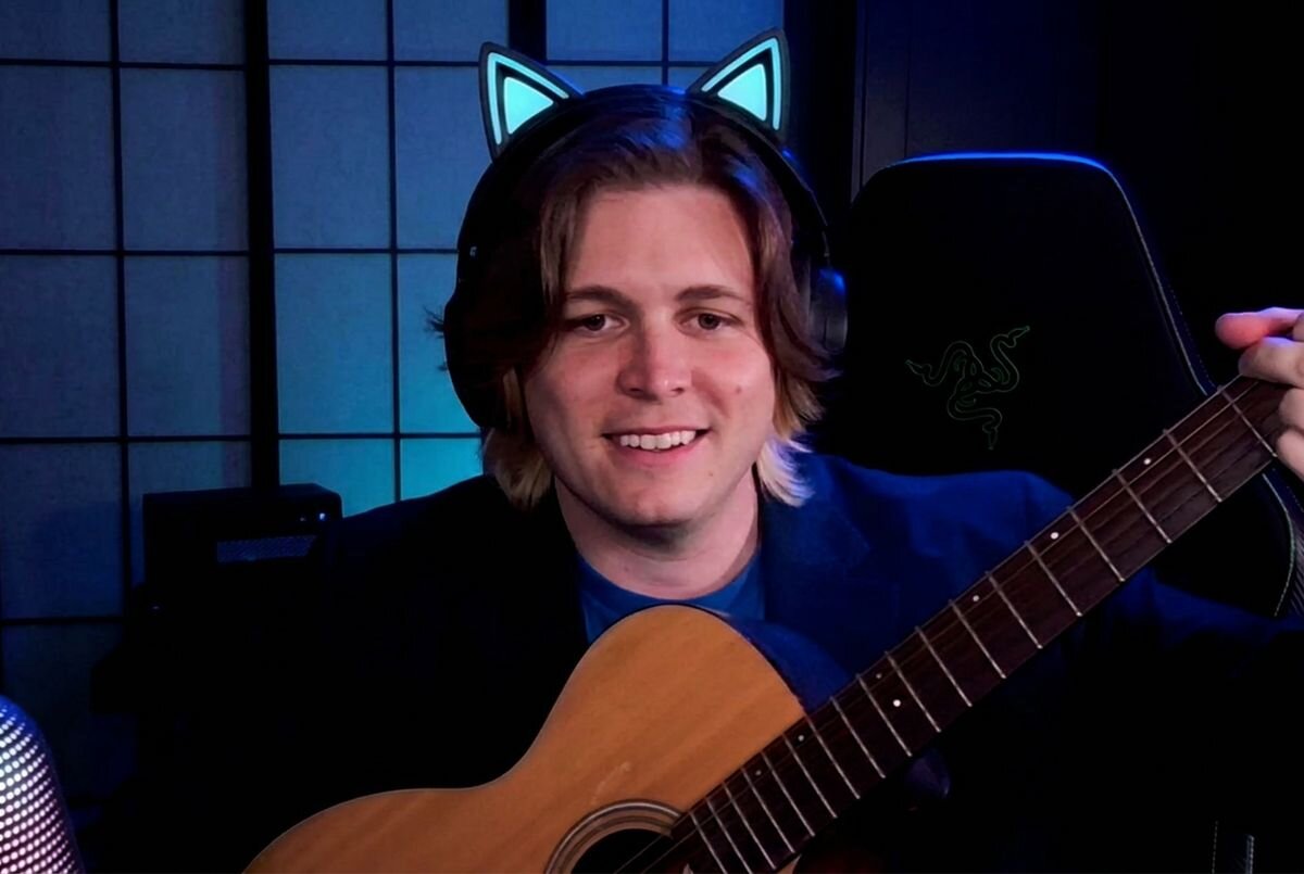 RAZER Kiyo V2 4K Automatyczne kadrowanie sztucznej inteligencji Inteligentne efekty obrotu, pochylenia i zoomu - Mężczyzna w słuchawkach z uszami kota grający na gitarze akustycznej przed kamerą