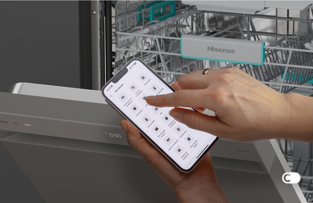 Osoba obsługuje smartfon z aplikacją przed otwartą zmywarką, na której widoczne jest logo \'Hisense\'.