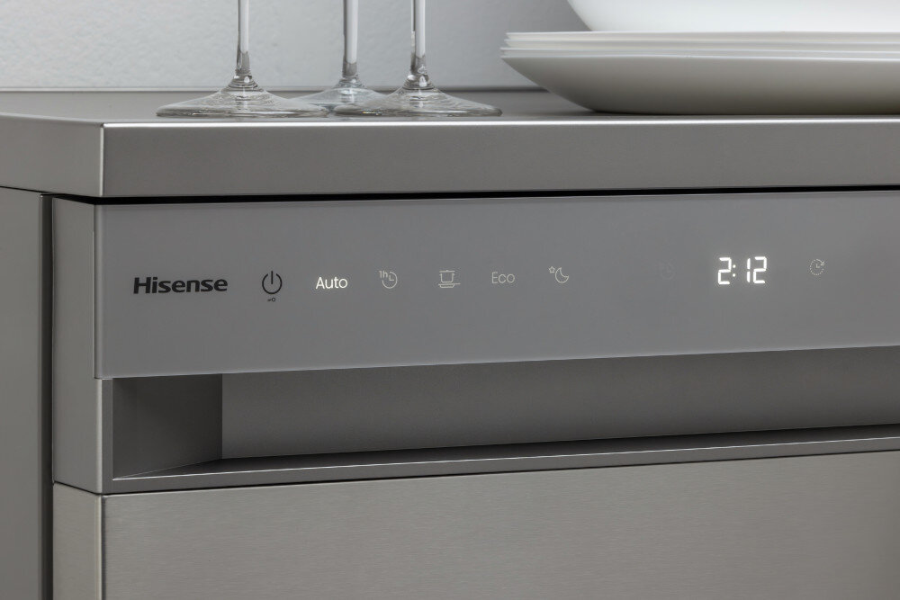 ZMYWARKA HISENSE HS693A90XAD Zbliżenie na przedni panel zmywarki Hisense pokazuje podświetlane ikonki programów, w tym Auto i Eco, oraz cyfrowy wyświetlacz z czasem 2:12 po prawej stronie. Na górnym blacie stoją kieliszki i biały talerz, co podkreśla elegancki charakter urządzenia program automatyczny czujniki zabrudzeń optymalne mycie