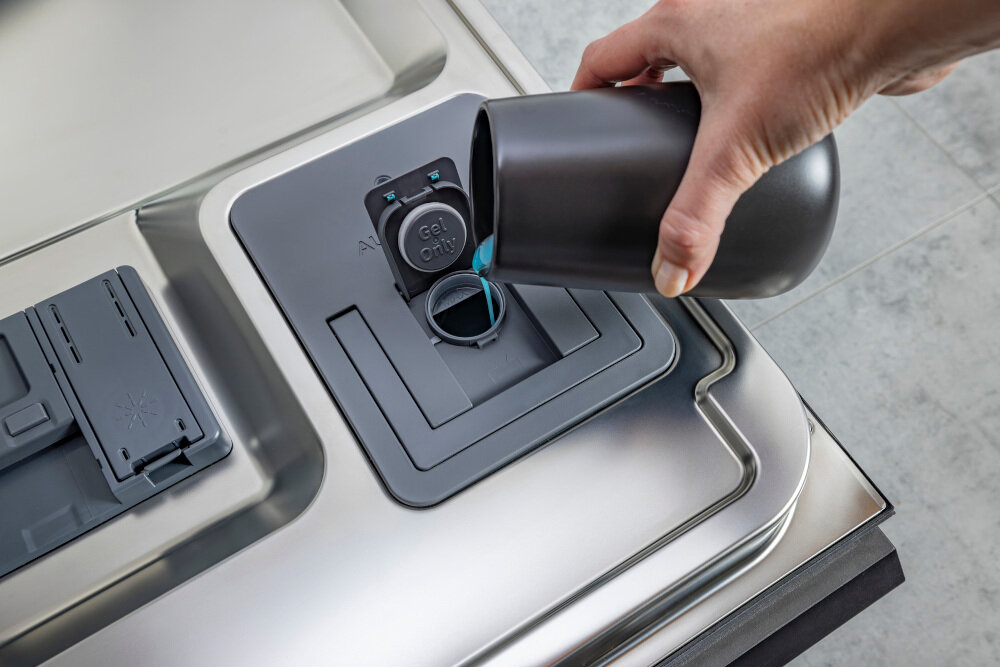 ZMYWARKA HISENSE HS693A90XAD Na zdjęciu widać rękę wlewającą niebieski płyn do specjalnego dozownika detergentu w dnie drzwi zmywarki, z klapką opisaną „Gel Only”. Obok znajduje się drugi, zamknięty pojemnik na nabłyszczacz lub tabletki, a całość otoczona jest stalową powierzchnią wnętrza automatyczne dozowanie detergentu oszczędność detergentu zbiornik 20 cykli