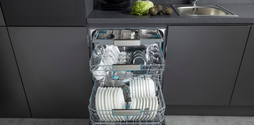 ZMYWARKA HISENSE HS693A90XAD Zmywarka zabudowana w ciemnej kuchni ma wysunięte wszystkie trzy kosze zapełnione naczyniami, garnkami i sztućcami. Na blacie obok zlewu ułożono warzywa, co tworzy realistyczne, domowe otoczenie 16 kompletów regulowane kosze pojemna zmywarka