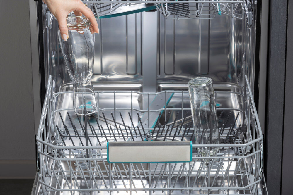 ZMYWARKA HISENSE HS693A90XAD Otwarty dolny kosz zmywarki wypełniony jest wysokimi butelkami szklanymi ustawionymi w specjalnych, turkusowych uchwytach. Z lewej strony widoczna jest dłoń wkładająca kolejną butelkę, co podkreśla wygodne mycie wysokich naczyń mycie butelek precyzyjny strumień dysza czyszcząca