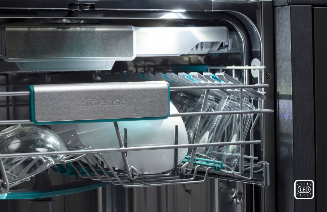 Wnętrze zmywarki z widocznymi szklankami i talerzami na metalowych półkach. Na uchwycie widnieje napis \'Hisense\'.