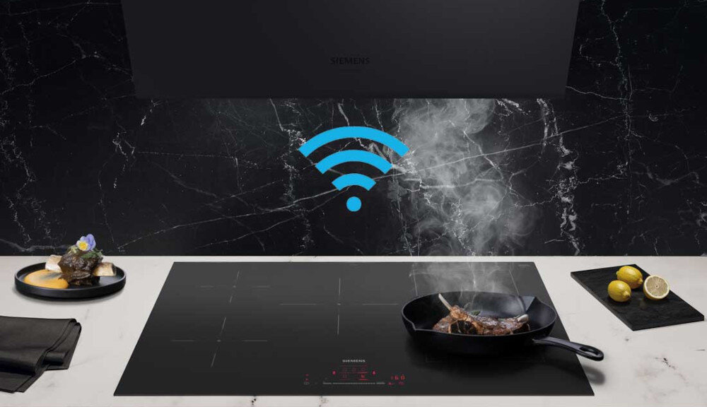 PŁYTA SIEMENS ED81AHWB1E 4.jpg przedstawia czarną płytę indukcyjną, na której stoi żeliwna patelnia z wysmażanym mięsem, unoszącą się parą. Nad płytą, na tle czarnej, marmurkowej ściany i pod okapem Siemens, umieszczono niebieską ikonę Wi‑Fi symbolizującą bezprzewodowe połączenie płyty z okapem lub innym systemem smart home. Po bokach blatu widoczne są elegancko podane dania oraz deska z cytrynami, co podkreśla, gastronomiczny charakter aranżacji okap Siemens automatyczne sterowanie okapem inteligentna płyta grzewcza kuchnia bez zapachów automatyczne włączanie okapu connected cooking Siemens okap kuchenny premium