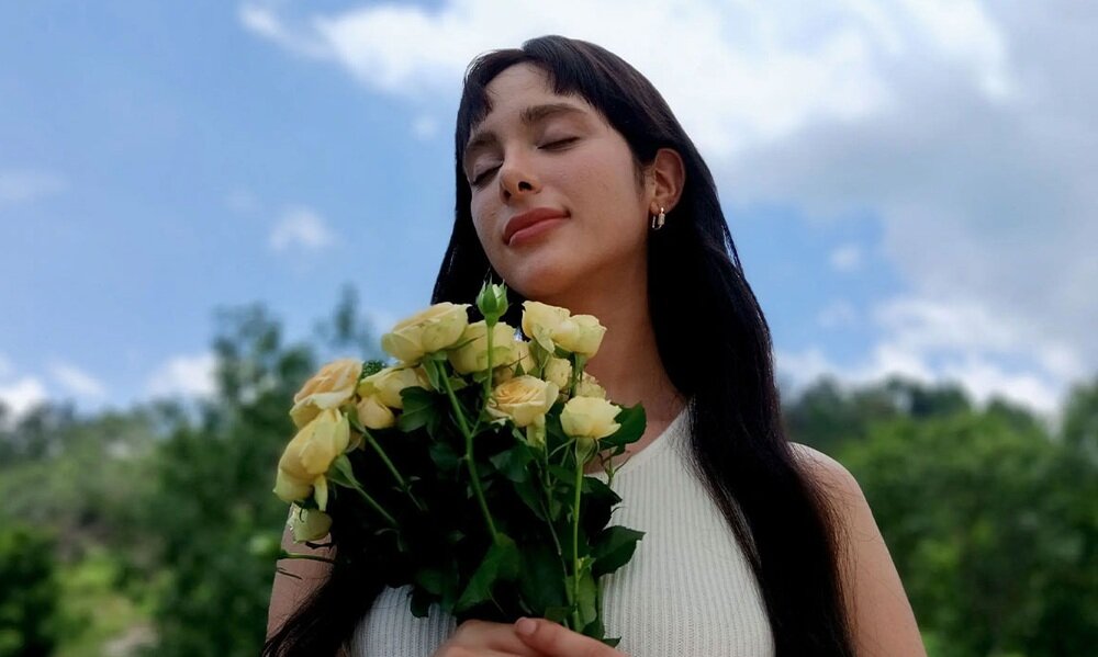 Kobieta z bukietem żółtych róż w plenerze, zdjęcie wykonane w trybie portretowym OPPO A6 Pro 5G.