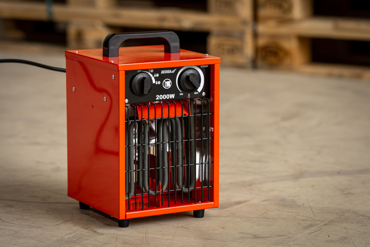 Nagrzewnica elektryczna DEDRA DED9920, 2000W, 320m³/h, równomierne, powierzchnia, Ręce regulują pokrętło temperatury na panelu nagrzewnicy DEDRA DED9920, widok z góry.