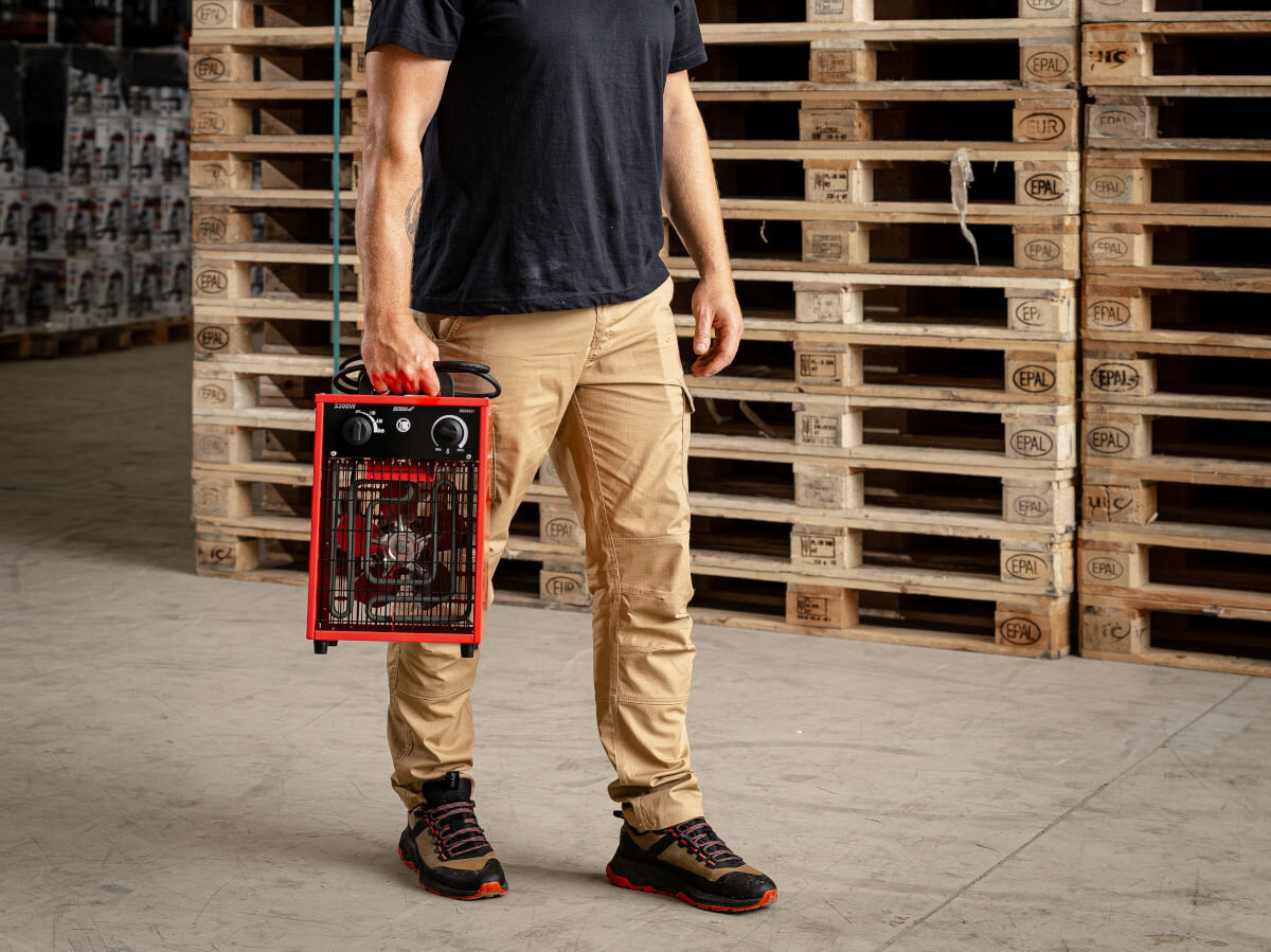 Nagrzewnica elektryczna DEDRA DED9921, uchwyt, lekkość, nóżki, ergonomia, Mężczyzna niesie nagrzewnicę DEDRA DED9921 w hali magazynowej, wyeksponowany front urządzenia.