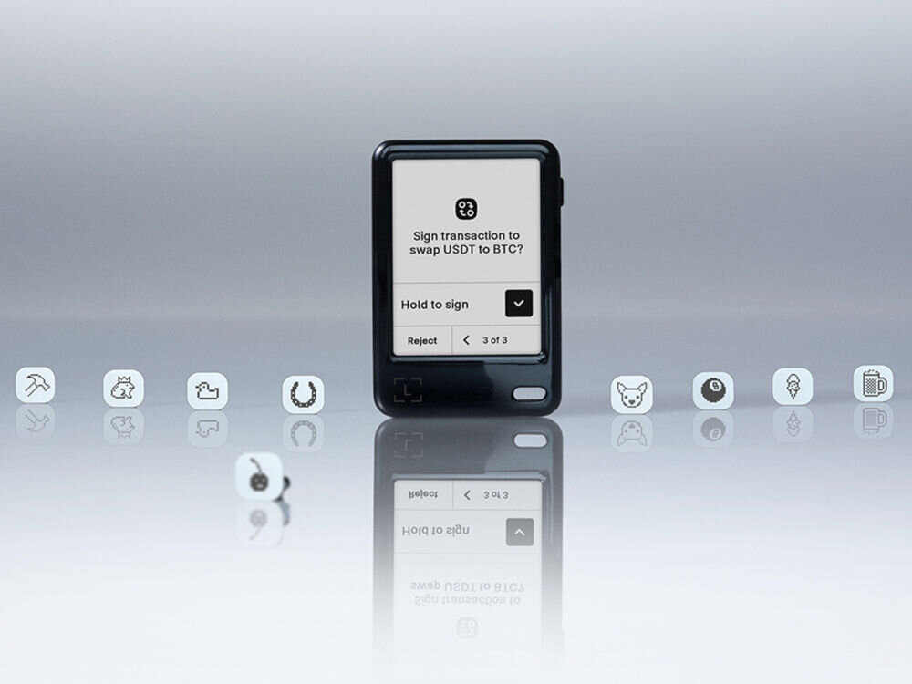 Portfel kryptowalut LEDGER Nano Gen5 Czarny portfel sprzętowy Ledger Nano z ekranem, umieszczony na lśniącej, szarej powierzchni. Na ekranie widoczna jest prośba o potwierdzenie transakcji: Sign transaction to swap USDT to BTC? z opcjami Hold to sign i Reject. Wokół urządzenia, po obu stronach, leżą małe, białe kostki z piktogramami, symbolizującymi różne funkcje lub aplikacje.