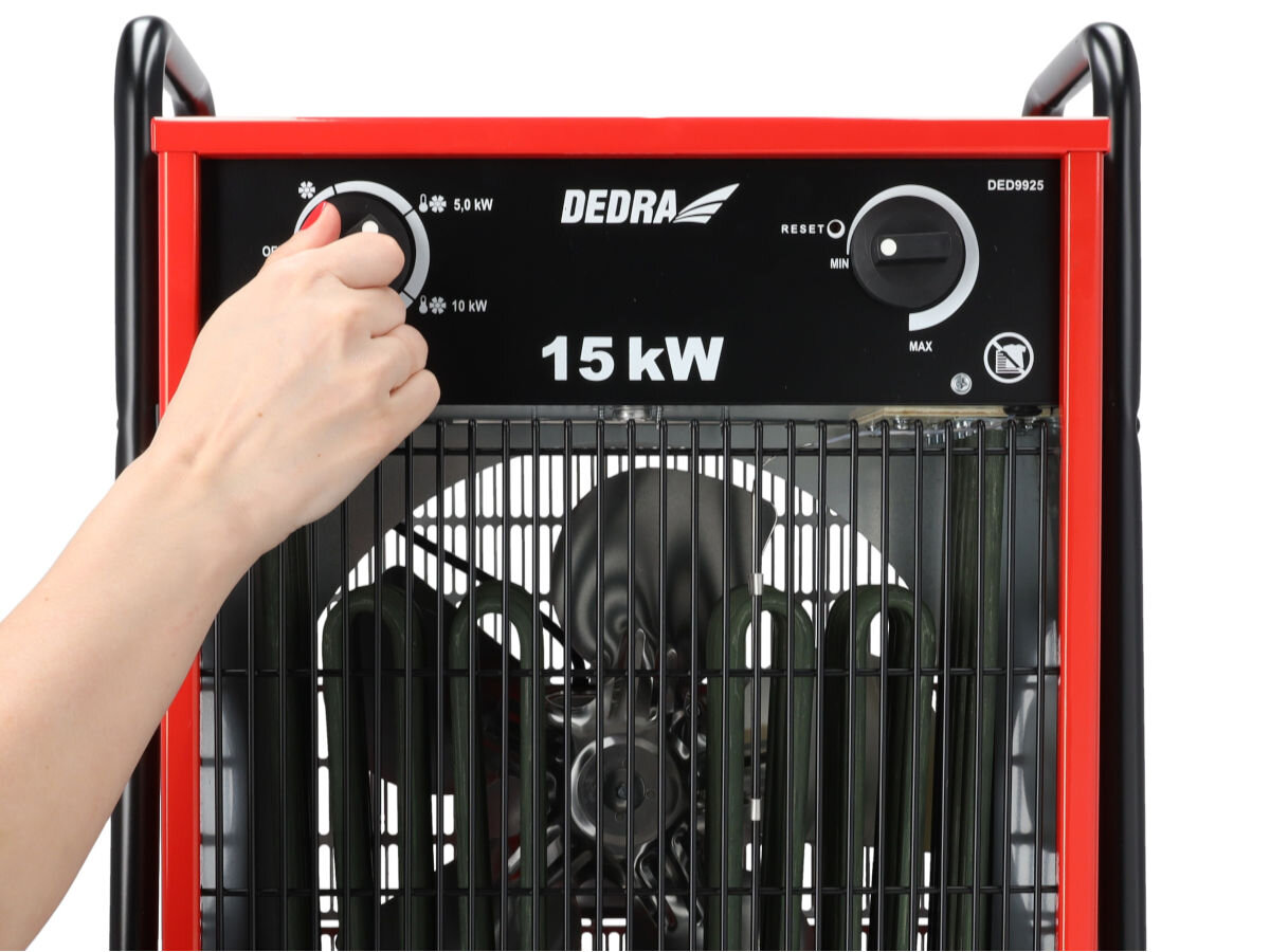 Nagrzewnica elektryczna DEDRA DED9925, termostat, płynność, wentylator, całoroczność, Ręka ustawia tryb pracy na pokrętle nagrzewnicy 15 kW, centralnie widoczny wentylator.