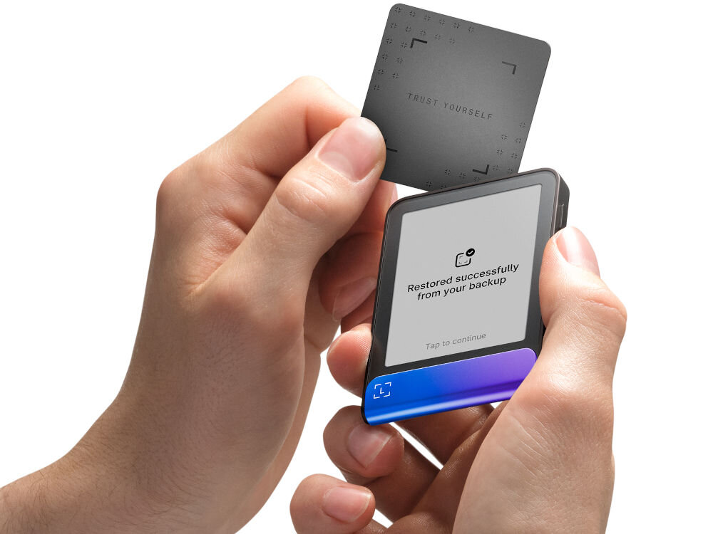 Portfel kryptowalut LEDGER Flex Ręce trzymają Ledger Stax oraz zbliżają do niego Ledger Recover Card (kartę do odzyskiwania). Na ekranie urządzenia widać komunikat: Restored successfully from your backup. Zielono-turkusowy pasek na dole ma animowany symbol potwierdzenia w kształcie nawiasów.