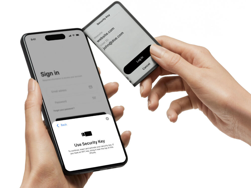 Portfel kryptowalut LEDGER Stax Crypto Hardware Wallet + Klucz odzyskiwania Dłonie trzymają smartfon i portfel sprzętowy Ledger Stax. Smartfon wyświetla ekran logowania (Sign in) i prosi o użycie klucza bezpieczeństwa (Use Security Key). Urządzenie Ledger Stax, używane jako klucz bezpieczeństwa NFC, wyświetla prośbę o zalogowanie się do serwisu (Website) z użyciem ID użytkownika (john@doe.com) i przyciskiem 