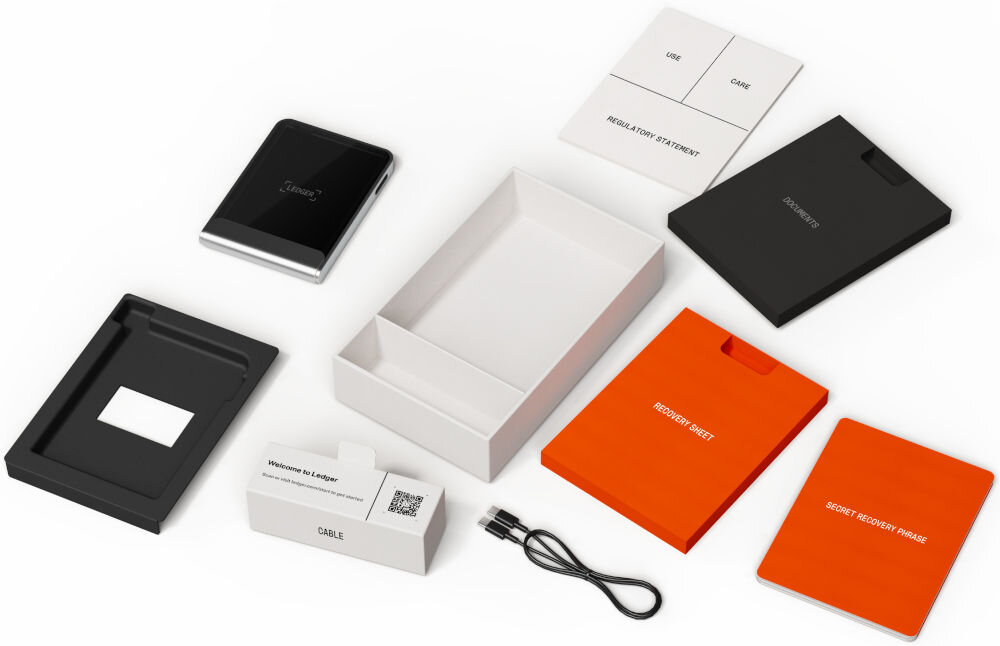 Portfel kryptowalut LEDGER Flex Widok rozłożonego zestawu i zawartości opakowania Ledger Stax. Wśród elementów znajdują się: sam portfel sprzętowy Ledger Stax, pudełka, kabel USB, instrukcje i dokumenty, w tym Recovery Sheet (arkusz odzyskiwania), SECRET RECOVERY PHRASE (tajna fraza odzyskiwania), oraz mała czarna karta z napisem RECOVERY KEY.