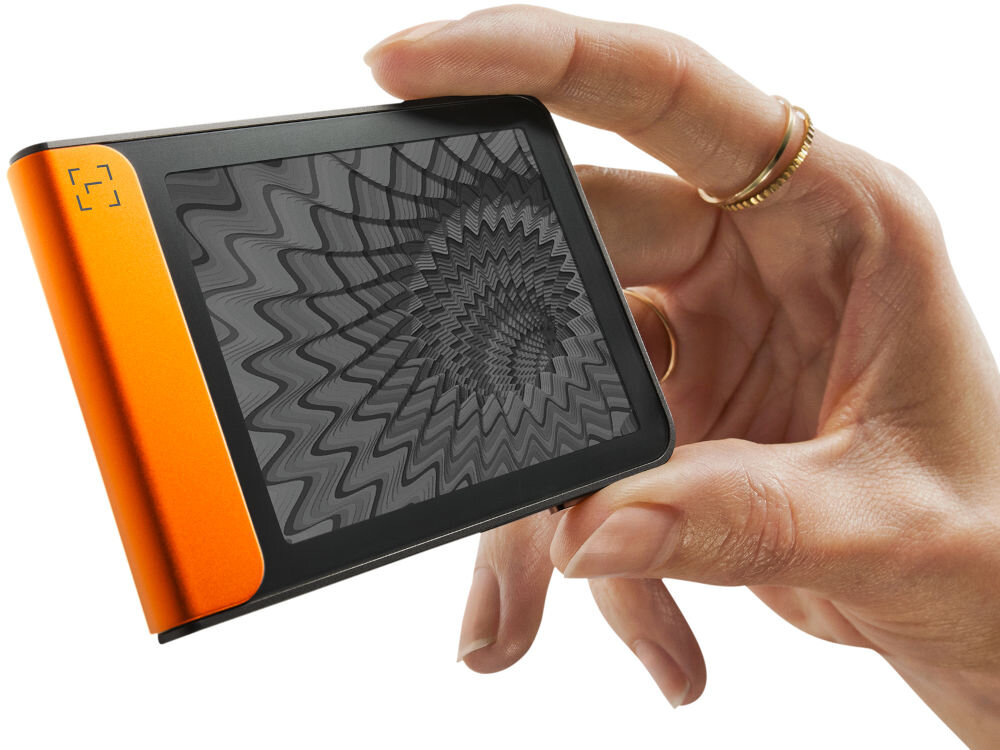 Portfel kryptowalut LEDGER Flex Zbliżenie na Ledger Stax trzymany w dłoni, pokazujące dynamiczną grafikę o hipnotycznym, falistym wzorze na ekranie e-ink (papier elektroniczny). Urządzenie jest zwrócone bokiem, eksponując jasny zielono-turkusowy element.