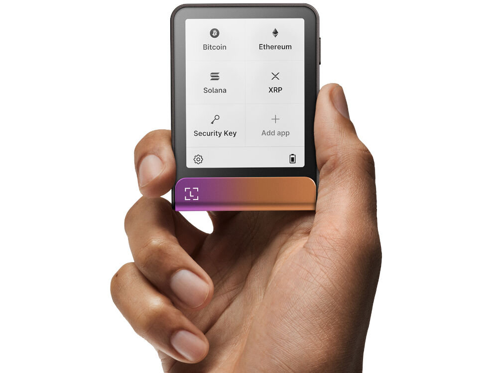 Portfel kryptowalut LEDGER Flex Ledger Stax stoi na drewnianym blacie obok szklanego kubka z kawą i pęku kluczy. Na ekranie urządzenia widnieje komunikat: Restored successfully from your backup (Pomyślnie przywrócono z kopii zapasowej) z opcją Tap to continue (Dotknij, aby kontynuować). Obok leży Ledger Recover Card.