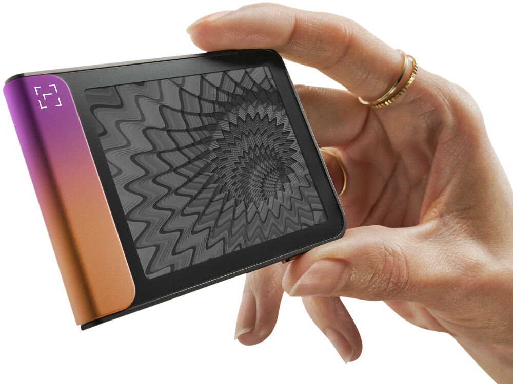 Portfel kryptowalut LEDGER Flex Zbliżenie na Ledger Stax trzymany w dłoni, pokazujące dynamiczną grafikę o hipnotycznym, falistym wzorze na ekranie e-ink (papier elektroniczny). Urządzenie jest zwrócone bokiem, eksponując jasny zielono-turkusowy element.
