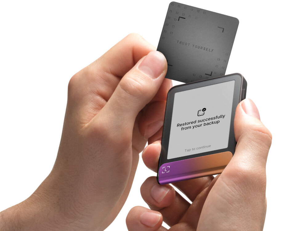 Portfel kryptowalut LEDGER Flex Ręce trzymają Ledger Stax oraz zbliżają do niego Ledger Recover Card (kartę do odzyskiwania). Na ekranie urządzenia widać komunikat: Restored successfully from your backup. Zielono-turkusowy pasek na dole ma animowany symbol potwierdzenia w kształcie nawiasów.