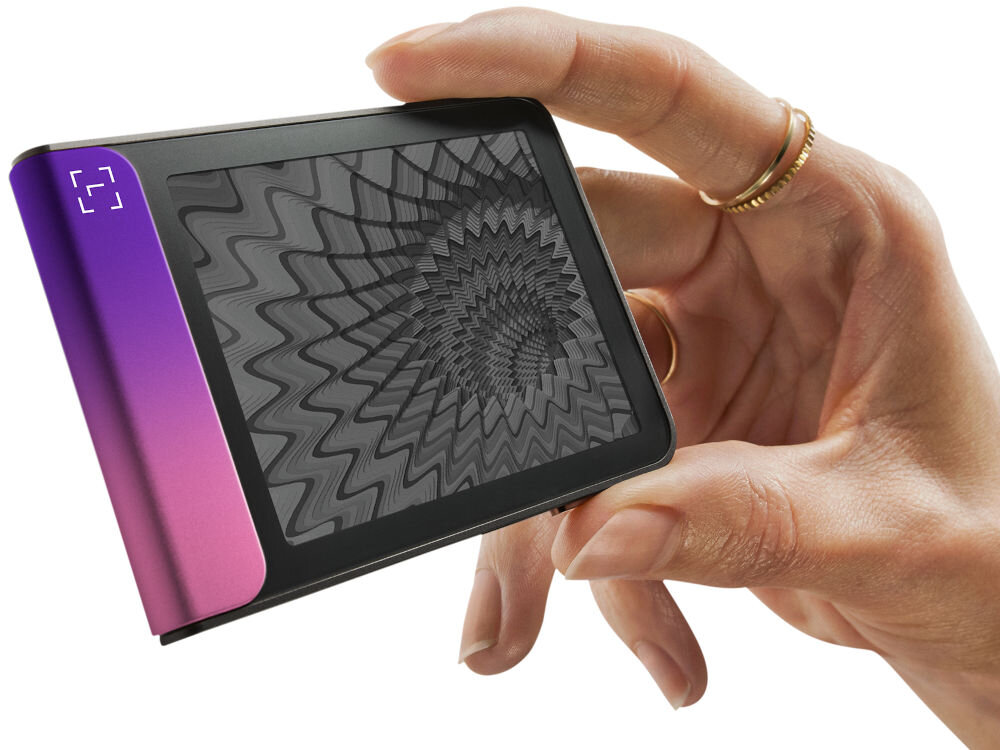 Portfel kryptowalut LEDGER Flex Zbliżenie na Ledger Stax trzymany w dłoni, pokazujące dynamiczną grafikę o hipnotycznym, falistym wzorze na ekranie e-ink (papier elektroniczny). Urządzenie jest zwrócone bokiem, eksponując jasny zielono-turkusowy element.