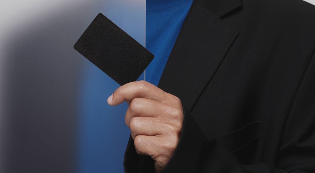 Osoba trzyma kartę Tangem w dłoni na tle przejścia z ciemnego do jasnego niebieskiego.  