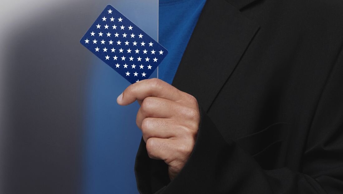 Osoba trzyma kartę Tangem w dłoni na tle przejścia z ciemnego do jasnego niebieskiego.  