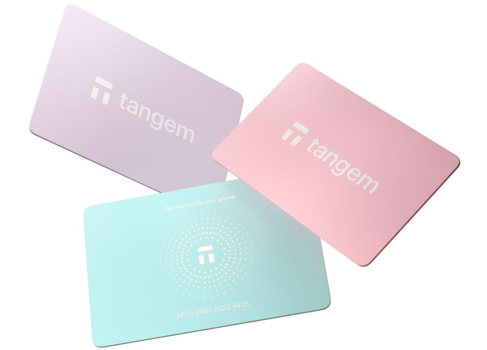 Pastelowe karty Tangem w kolorach fioletowym, różowym i turkusowym są ułożone wachlarzowo na białym tle - portfel kryptowalutowy w formie trzech kart 
