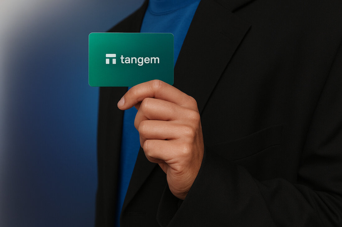 Osoba trzyma kartę Tangem w dłoni na tle przejścia z ciemnego do jasnego niebieskiego.  