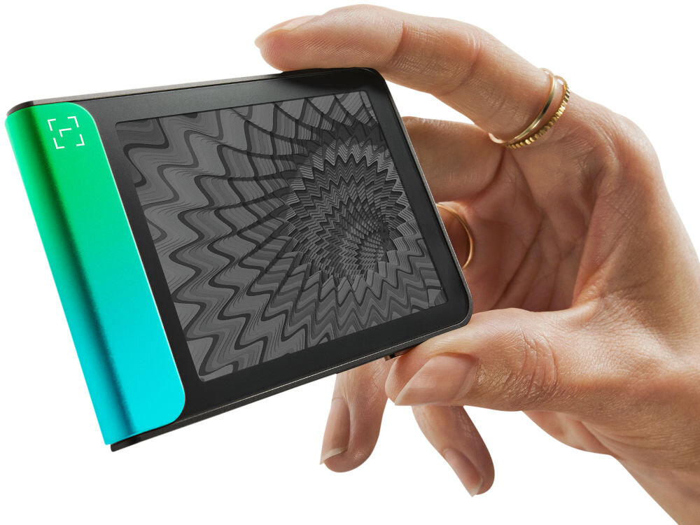 Portfel kryptowalut LEDGER Flex Zbliżenie na Ledger Stax trzymany w dłoni, pokazujące dynamiczną grafikę o hipnotycznym, falistym wzorze na ekranie e-ink (papier elektroniczny). Urządzenie jest zwrócone bokiem, eksponując jasny zielono-turkusowy element.