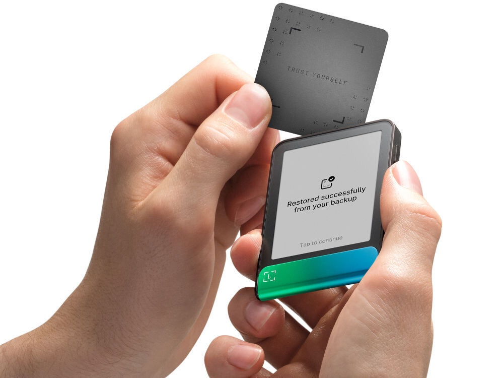 Portfel kryptowalut LEDGER Flex Ręce trzymają Ledger Stax oraz zbliżają do niego Ledger Recover Card (kartę do odzyskiwania). Na ekranie urządzenia widać komunikat: Restored successfully from your backup. Zielono-turkusowy pasek na dole ma animowany symbol potwierdzenia w kształcie nawiasów.