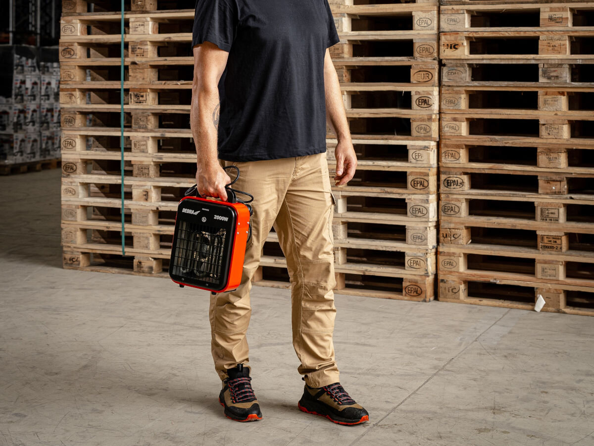 Nagrzewnica elektryczna DEDRA DED9920B, uchwyt, ergonomia, obsługa, lekkość, Mężczyzna przenosi nagrzewnicę Dedra DED9920B w magazynie, widok urządzenia typu slim.
