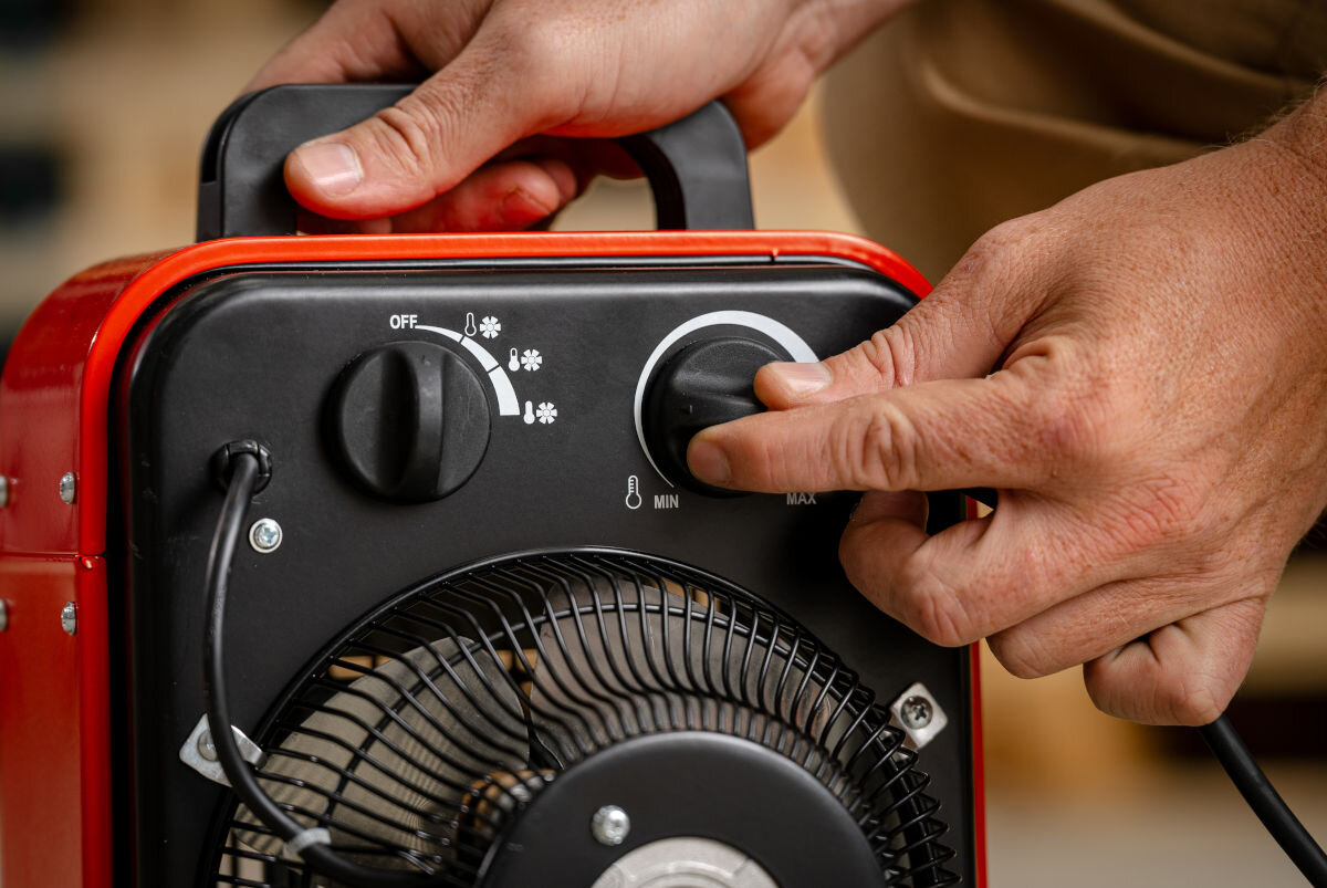 Nagrzewnica elektryczna DEDRA DED9921B, termostat, oszczędność, płynność, ekonomia, Ręka reguluje pokrętło temperatury na panelu nagrzewnicy DED9921B podczas pracy urządzenia.