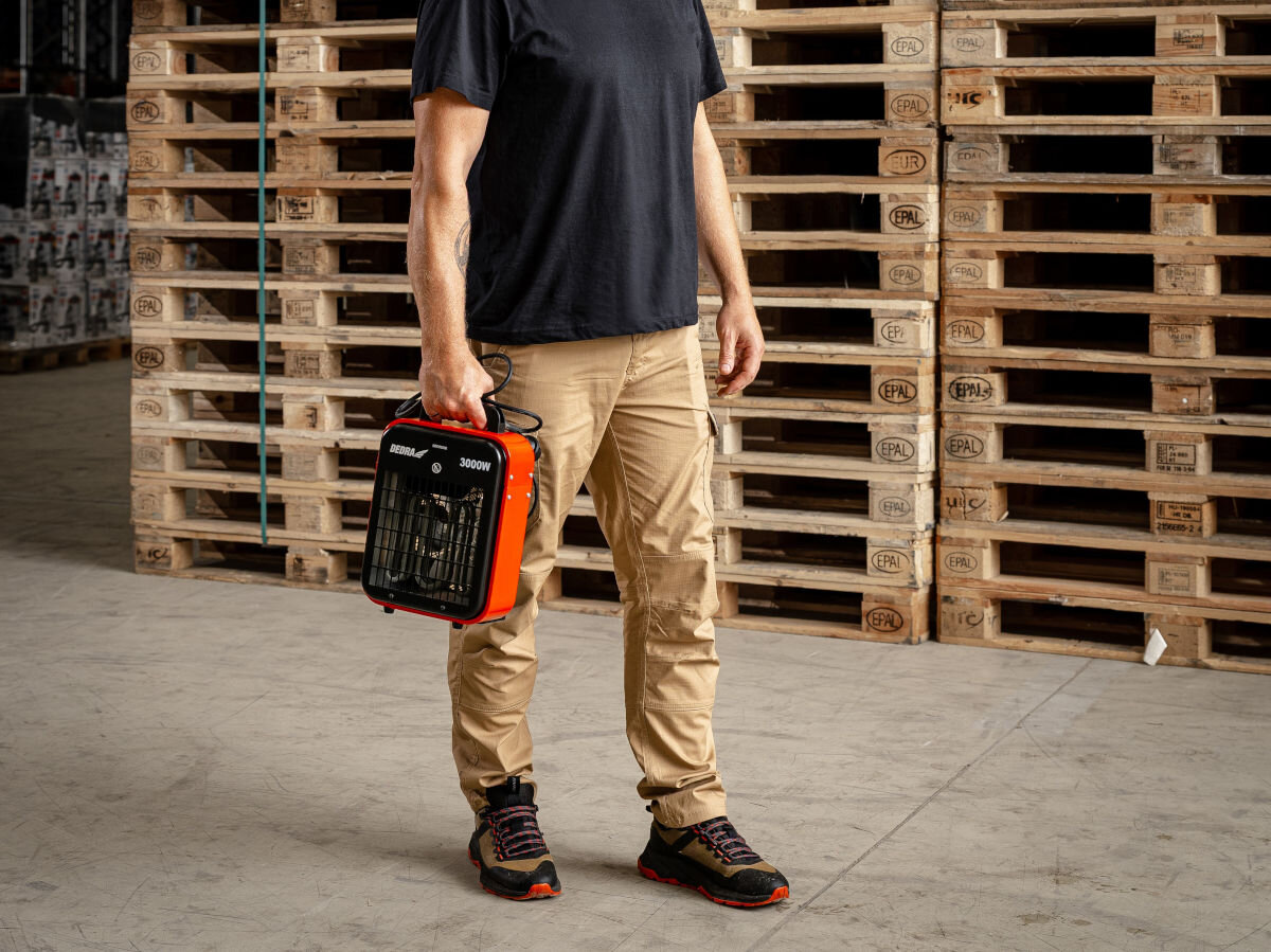 Nagrzewnica elektryczna DEDRA DED9921B, lekkość, uchwyt, ergonomia, mobilność, Mężczyzna niesie nagrzewnicę DED9921B w hali magazynowej, urządzenie gotowe do transportu.