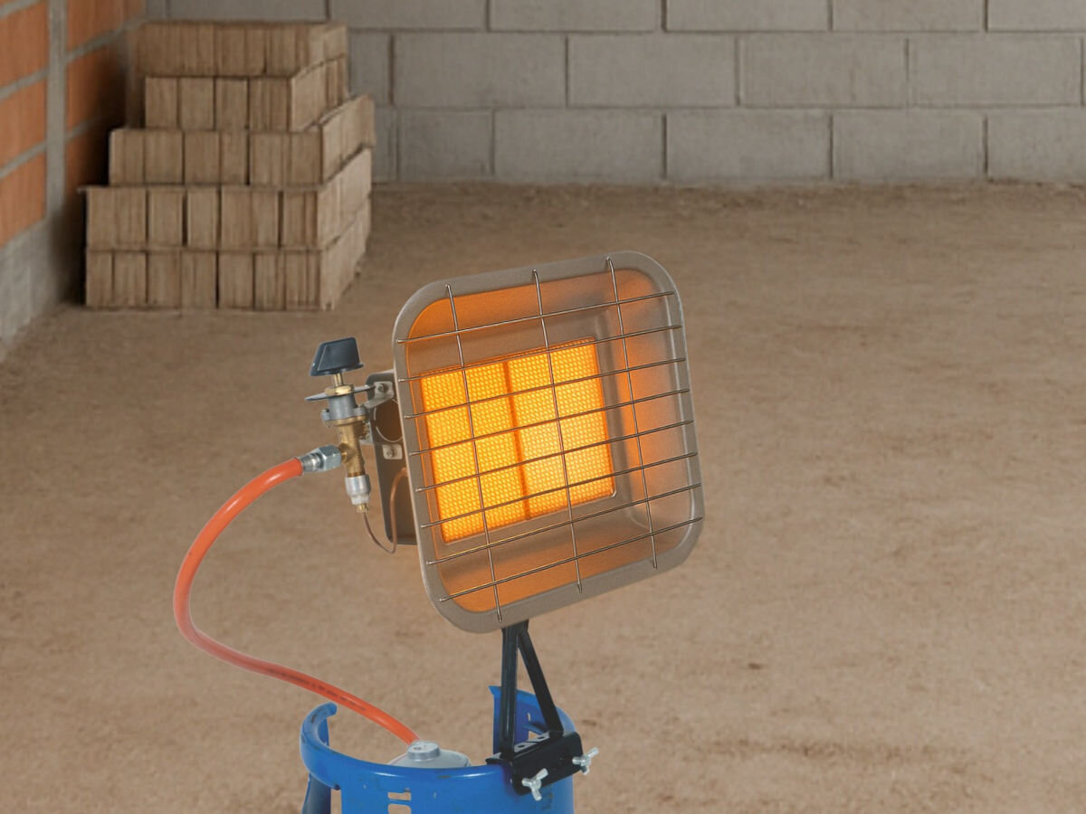 Promiennik DEDRA DED9970, 4,6kW, 37mbar, 340g/h, efektywność, Pracujący promiennik DED9970 na butli, w pomieszczeniu, ceglana ściana, paczka cegieł.