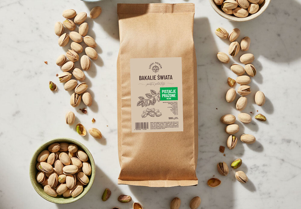 Pistacje prażone CABRAL (1 kg) marmurowy blat opakowanie mieszanki leży na blacie wokół miseczki wypełnione pistacjami komponują się z owsianką jogurtem domową granolą pełny naturalny smak i przyjemna chrupkość w wypiekach i deserach dodają wyrazistości sałatkom makaronom deską serów delikatna nuta